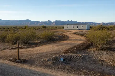 Fresh-bladed dirt driveway curving through creosote toward a home site on Buckeye desert acreage with a culvert set at the wash crossing