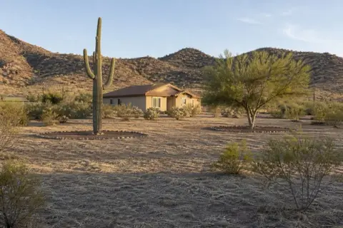 Wide defensible-space ring mowed to stubble around a stucco home on a desert-edge Buckeye lot with a preserved saguaro inside the ring