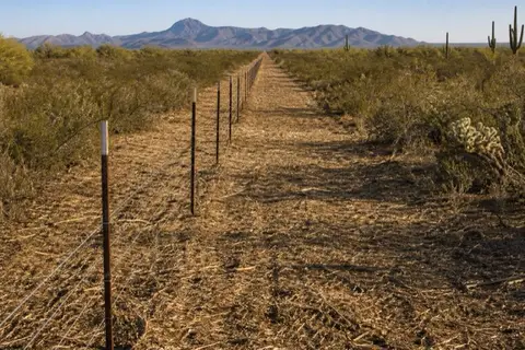 Freshly cleared straight corridor along a rural five-strand wire fence near Buckeye running toward the White Tank Mountains