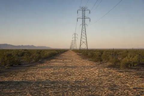 Long mulched utility easement running straight across open desert west of Buckeye with steel transmission towers marching toward the horizon