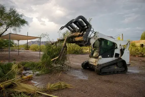 Skid-steer grapple loading a wind-snapped tree limb on a Buckeye ranchette the morning after a monsoon storm